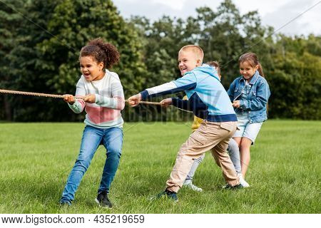 childhood, leisure and people concept - group of happy kids playing tug-of-war game and running at park