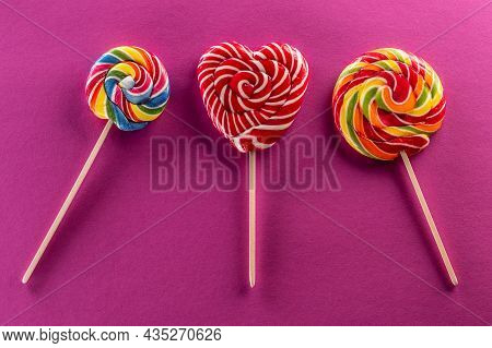 Set Of Three Lollipops With Rainbow Colour And Fruit Flawor With Purple Background.