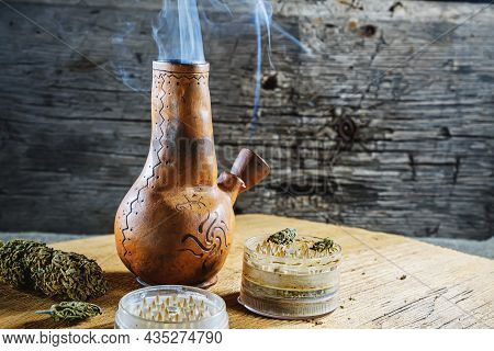 Old Brown Steamung Bong And Open Cannabis Grinder With Chopped Marijuana Weed And Medical Cannabis I