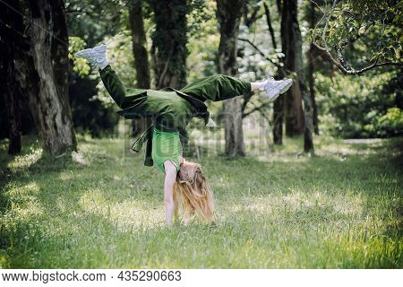 A Girl In A Green Outfit Makes A Flip On Her Arms On A Summer Lawn In A Parkgreen Outfit Makes A Fli