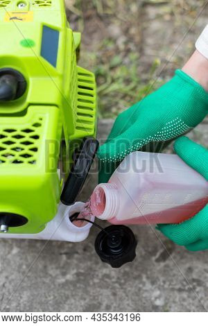 Hands In Gloves Filling The Grass Cutter Mower With Gasoline Petrol From Plastic Can