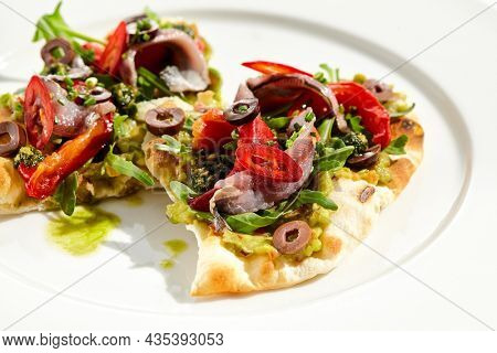 Tapas with avocado cream, anchovy, paprika and kalamata olives on focaccia. Bruschetta with guacamole and anchovy isolated on white background. Appetizer contemporary concept. Fish antipasti