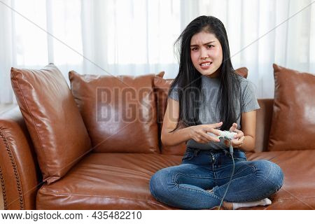 Vdo Game Console Station Concept. Active Asian Woman Sitting On Sofa, Holding Joystick And Playing E
