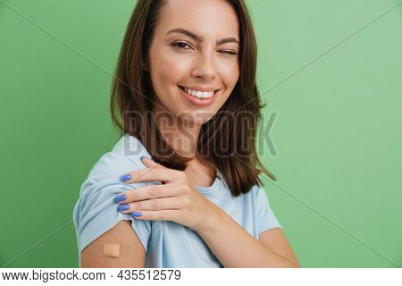 Young brunette woman winking while showing her bandage isolated over green background