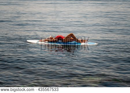 Sporty Girl On A Glanders Surfboard In The Sea On A Sunny Summer Day. In A Striped Swimsuit, He Lies