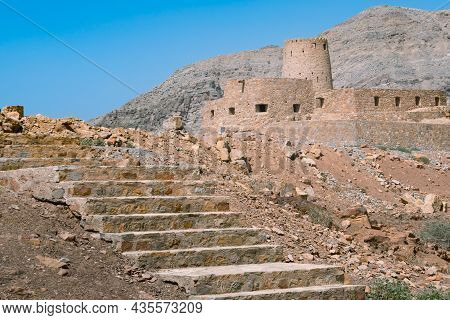 Stone Walls Of Small Medieval Arabian Fort Under Tall Mountain Cliffs. Fortress In Bukha, Musandam P