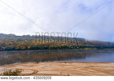 A View Of The River Between Two Banks, A Fisherman On The Shore And In A Boat, A Colorful Forest On 