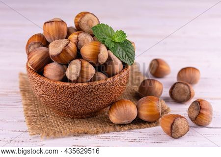Hazelnuts In Shells In A Wooden Bowl On A White Wooden Background. Close-up.