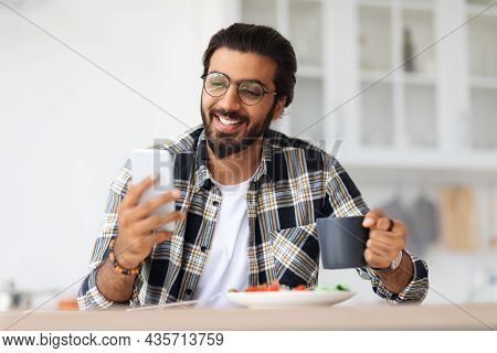 Smiling Idian Man Eating Healthy Food And Using Phone