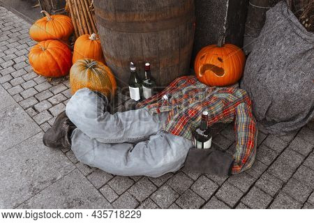Pumpkin Man Laying On Sidewalk With Liquor Bottles. Creative Halloween Party Outside Decoration. Hel