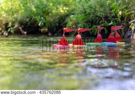Sports Regatta Of Children's Toy Ships On The Creek. Five Homemade Mast Boats Floating On The Water 