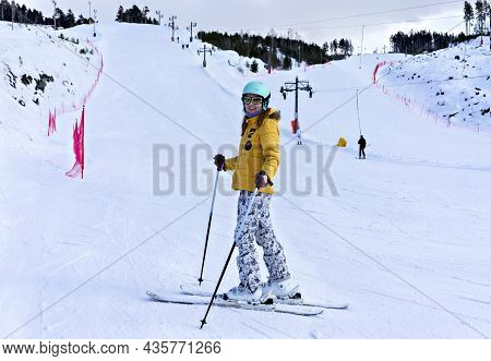 Happy Smiling Young Woman In Yellow Jacket And Ski Helmet Downhill Skiing On A Mountain Slope, Winte