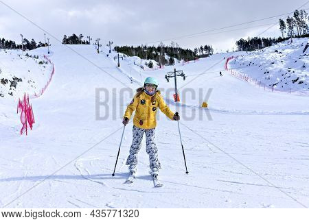 Happy Smiling Young Woman In Yellow Jacket And Ski Helmet Skiing On A Mountain Slope, Winter Sports,