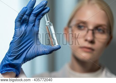 A Woman Scientist In Strict Glasses Holds An Apmula With A Vaccine In Front Of Her Face. Development