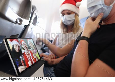 Man And Woman Wearing Protective Masks And Santa Claus Hats Flying In Airplane And Having Conference