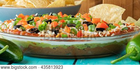 A Narrow View Of A Homemade 7 Layer Dip With One Tortilla Chip Sticking Out.
