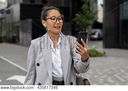 Happy young businesswoman makig video call while walking alone contemporary buildings