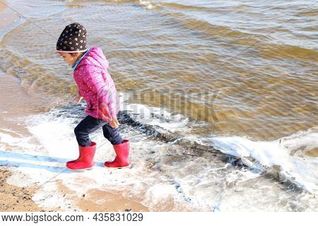 Child Girl Playing By The Sea In Autumn. A Girl In A Red Jacket In A Beautiful Autumn On The Seashor