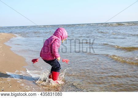 Child Girl Playing By The Sea In Autumn. A Girl In A Red Jacket In A Beautiful Autumn On The Seashor