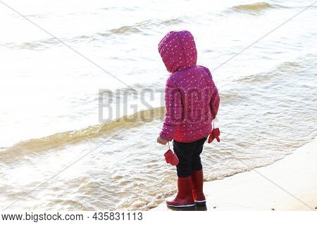 Child Girl Playing By The Sea In Autumn. A Girl In A Red Jacket In A Beautiful Autumn On The Seashor