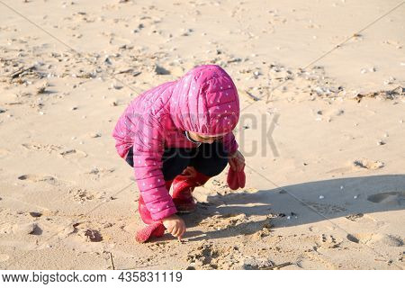 Child Girl Playing By The Sea In Autumn. A Girl In A Red Jacket In A Beautiful Autumn On The Seashor