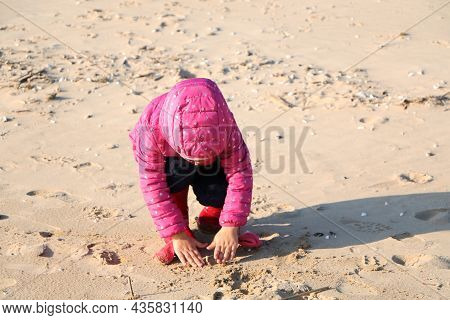 Child Girl Playing By The Sea In Autumn. A Girl In A Red Jacket In A Beautiful Autumn On The Seashor