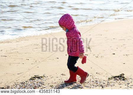 Child Girl Playing By The Sea In Autumn. A Girl In A Red Jacket In A Beautiful Autumn On The Seashor