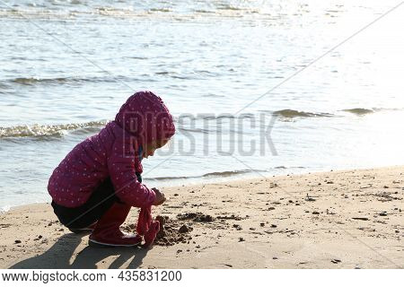 Child Girl Playing By The Sea In Autumn. A Girl In A Red Jacket In A Beautiful Autumn On The Seashor