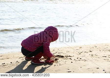 Child Girl Playing By The Sea In Autumn. A Girl In A Red Jacket In A Beautiful Autumn On The Seashor