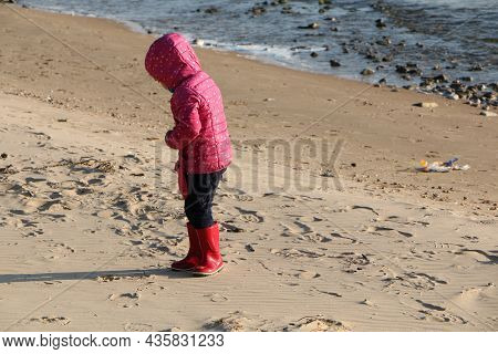 Child Girl Playing By The Sea In Autumn. A Girl In A Red Jacket In A Beautiful Autumn On The Seashor