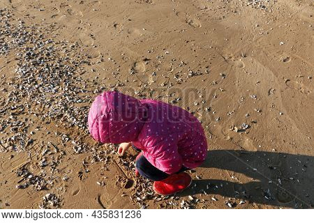 Child Girl Playing By The Sea In Autumn. A Girl In A Red Jacket In A Beautiful Autumn On The Seashor
