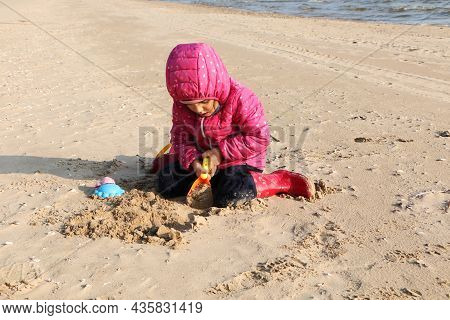 Child Girl Playing By The Sea In Autumn. A Girl In A Red Jacket In A Beautiful Autumn On The Seashor