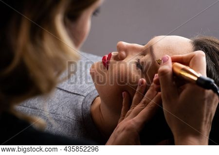 Young woman making tatouage for eyebrows in a dressing makeup room. Eyebrows make up process. Make-up artist in beauty studio doing makeup for beautiful girl. Making mua.