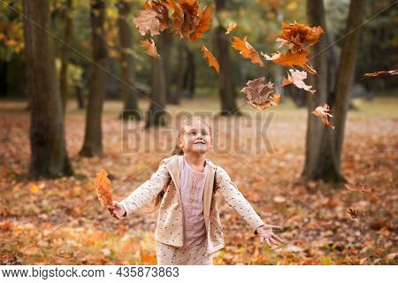 A Little Girl Tosses Leaves In A Praka In Autumn
