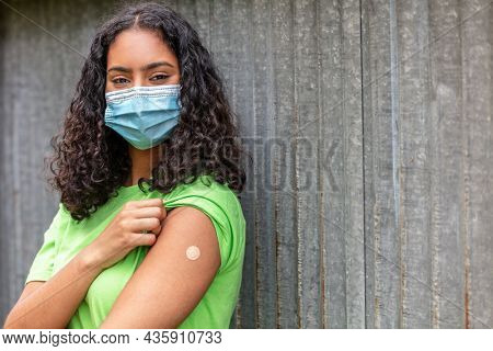 Vaccinated girl female young woman wearing face mask in Coronavirus COVID-19 pandemic showing vaccine sticking plaster