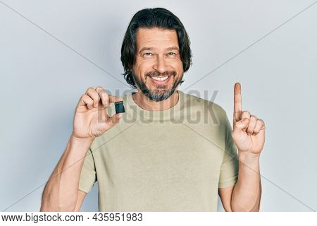 Middle age caucasian man holding sdxc card smiling with an idea or question pointing finger with happy face, number one 