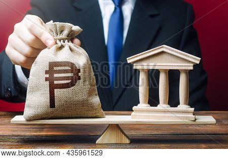 Man Puts A Philippine Peso Money Bag On Scales Next To A Bank. Taxes Payment. Lobbying Interests. St
