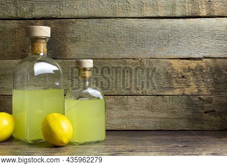 Two Bottles With Limoncello And Lemons With Copy Space On Rustic Wooden Background