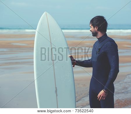 young professional surfer dressed in black wetsuit looking along the shore for find the perfect spot