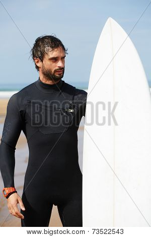Handsome surfer man in black diving suit holding his surfboard