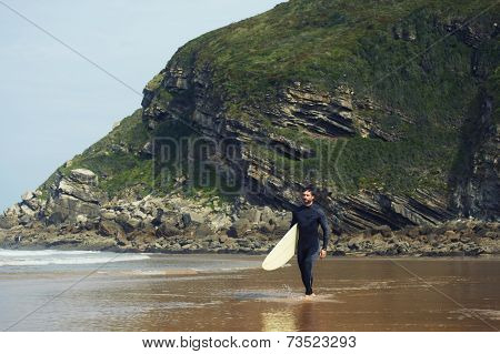 Young surfer walking to the waves along beautiful shore