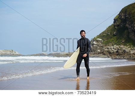 Young handsome surfer man walking with surfboard on the beach