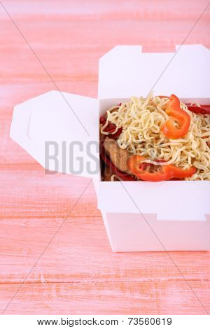 Chinese noodles with meat and pepper in takeaway box on pink background