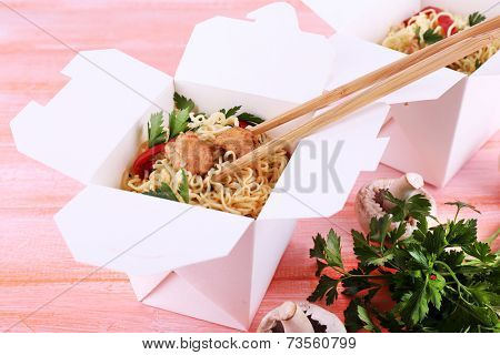 Chinese noodles with meat and pepper in takeaway boxes on pink background