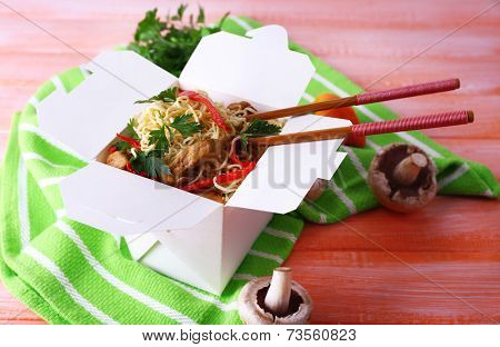 Chinese noodles and sticks in takeaway box on green napkin on pink background