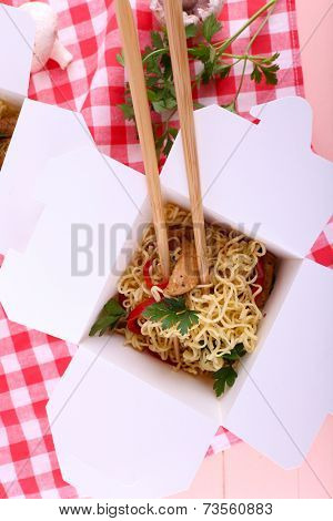 Chinese noodles and sticks in takeaway box on fabric background