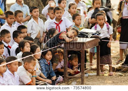 SAYABURY, LAOS, FEBRUARY 16, 2012: class of Laotian kids watching outdoor theater spectacle in the schoolyard during the Elefantasia festival in Sayaboury, Laos