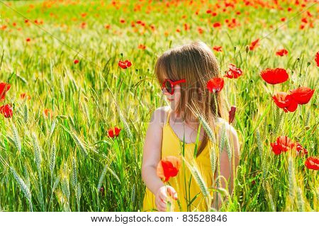 Summer portrait of a cute little girl playing in a poppy field on sunset