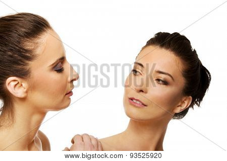 Two attractive topless sisters with make up looking at each other.