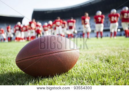 Close up of an american football on the field, players in the background